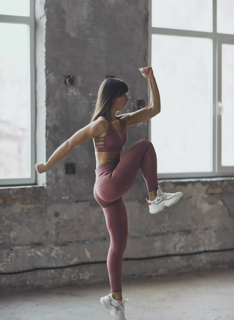 Mulher treinando em um estúdio, com o joelho elevado e o braço erguido